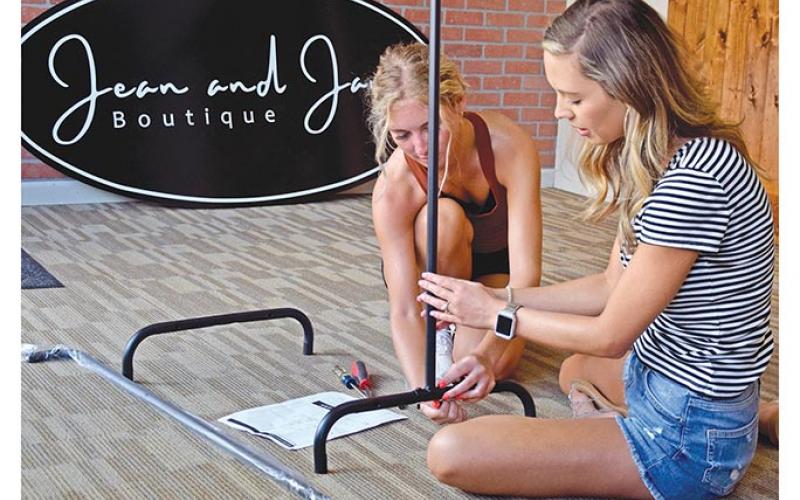 Macie Floyd and Madison Mason work together to assemble a clothing rack for their store, Jean and Jane Boutique, which is expected to open later this month. (Photo by Sinclair)