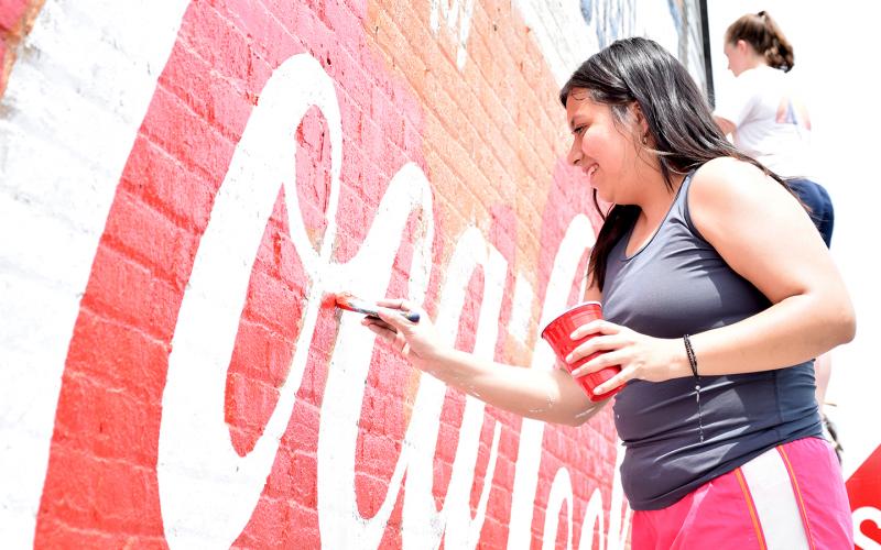 Alondra Arevalo carefully paints over the red around the white letters on the mural on West Main Street. (Photo by Sinclair)