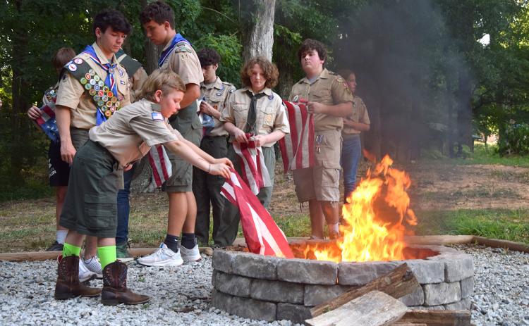 Cub Scout Noah Palmer carefully lowers part of an American flag into the fire pit beside the Lavonia Scout Hut as other Scouts watch. (Photo by Sinclair)