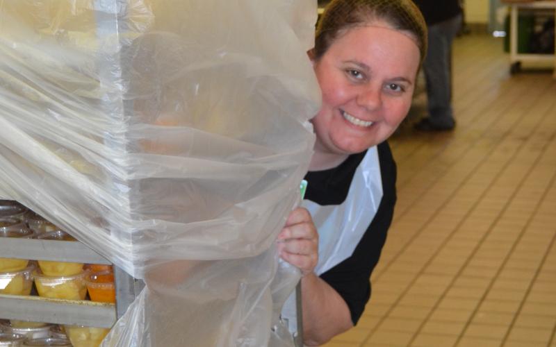 Michelle Jorschumb peeks from behind a cart as she and other members of the Lavonia Elementary School food nutrition service prepare to hand out meals Tuesday for students. (Photo by Eberhardt)