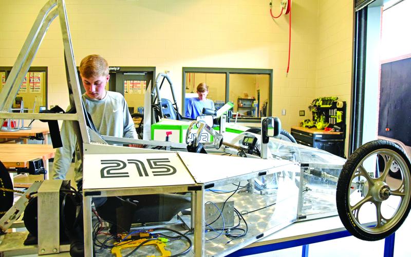 Ahead of their race in Rabun County, Rhett Floyd makes final adjustments on the new electric car with acrylic panels, while Landon Floyd works on the original electric car with corrugated panels.