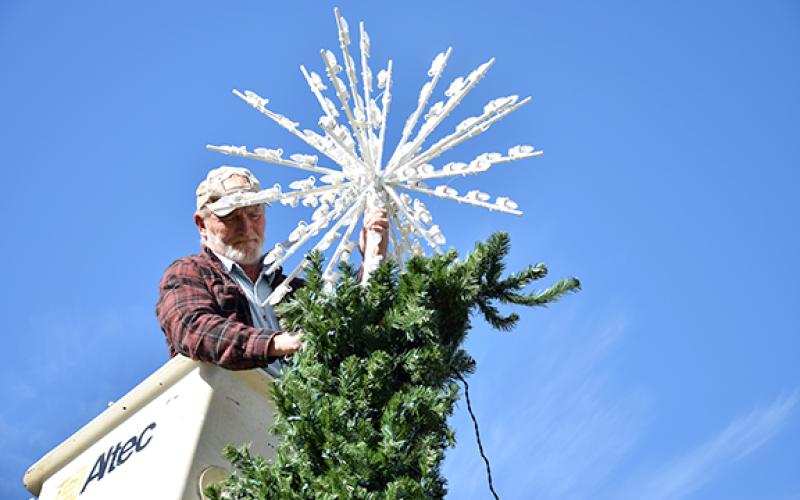 Kyle Paris works to place the star atop the Canon City Christmas tree in the city park last week. The city will hold its tree lighting service Sunday at 6 p.m. at the park. (Photo by Sinclair)