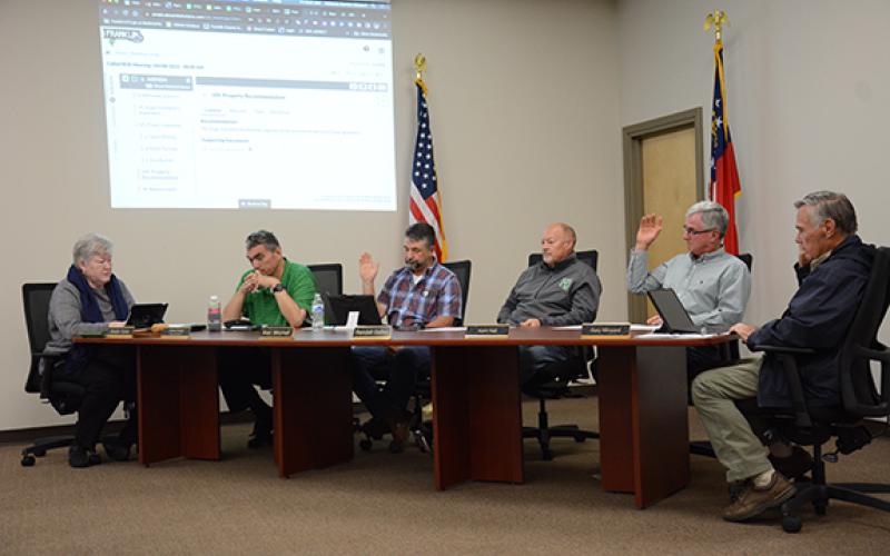 Franklin County Board of Education members Alan Mitchell, Kent Hall and Gary Minyard raise their hands to vote to purchase more than 120 acres of property just south of Carnesville as the site for a new school to replace Royston Elementary School. Fellow board members Robin Cato and Randall Gailey voted against the motion, as Superintendent Chris Forrer looked on. (Photo by Scoggins)