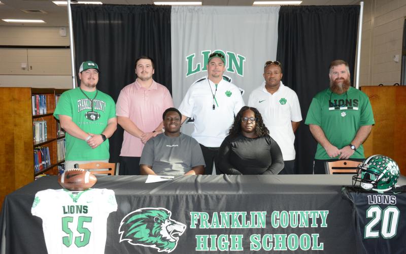 Antnez “Tank” Fortson (seated left) signed a college football scholarship to play for McPherson College in McPherson, Kan. Joining him at the signing ceremony at Franklin County High School last week were his mother, Breanda Fortson (seated right) and (back, from left) Franklin County Lion football coaches Caleb Hardy, Zach Marinell, Head Coach Chuck Holland, Robert Allen and Cayman Brooks. (Photo by Eavenson)