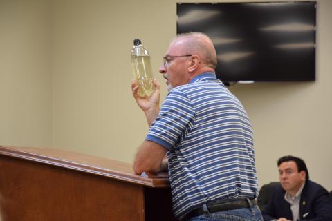 Mark Gibson shows county commissioners Monday a bottle of water taken from a polluted Indian Creek. (Photo by Scoggins)