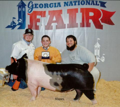 Devin Bowyer (center, with FCHS ag teacher Trey Harris at right) is one of the students who has benefited from being able to leave his pig project at the ag barn at Franklin County High School. Bowyer, one of the barn’s student managers, began showing pigs two years ago and won Senior Showmanship recently at the Georgia National Fair. A new ag barn that will allow more students to keep their pigs, sheep, goats and calves at school will be funded if voters choose to extend a special purpose local option sale