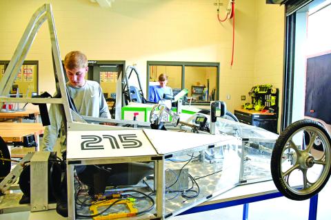 Ahead of their race in Rabun County, Rhett Floyd makes final adjustments on the new electric car with acrylic panels, while Landon Floyd works on the original electric car with corrugated panels.