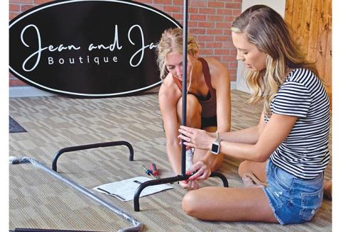 Macie Floyd and Madison Mason work together to assemble a clothing rack for their store, Jean and Jane Boutique, which is expected to open later this month. (Photo by Sinclair)