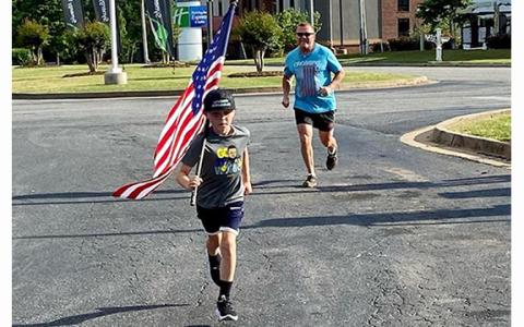 Shiloh Morgan carries the flag in front of his fa-ther Dusty during a Memorial Day run last year around Lavonia.