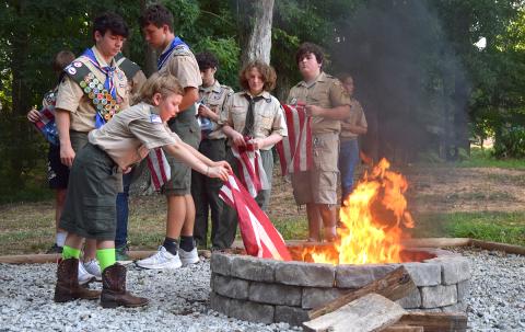 Cub Scout Noah Palmer carefully lowers part of an American flag into the fire pit beside the Lavonia Scout Hut as other Scouts watch. (Photo by Sinclair)