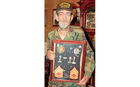 John McCollum holds a frame containing some his medals and patches from his service in the Vietnam War. (Photo by Scoggins)