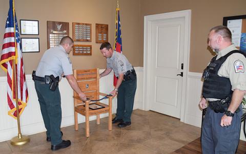 Georgia Department of Natural Resources officers place Capt. Stan Elrod’s honor chair between the flags in the lobby of Franklin Springs  City Hall as Officer-in-Charge Kevin Thompson looks on. (Photo by Sinclair)