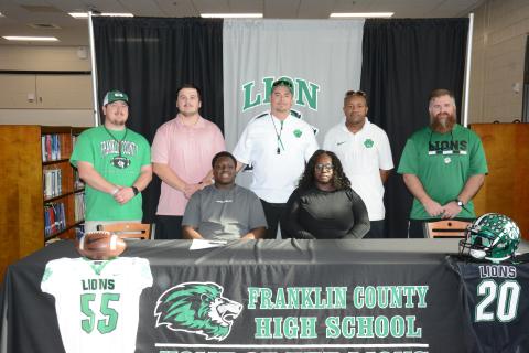 Antnez “Tank” Fortson (seated left) signed a college football scholarship to play for McPherson College in McPherson, Kan. Joining him at the signing ceremony at Franklin County High School last week were his mother, Breanda Fortson (seated right) and (back, from left) Franklin County Lion football coaches Caleb Hardy, Zach Marinell, Head Coach Chuck Holland, Robert Allen and Cayman Brooks. (Photo by Eavenson)