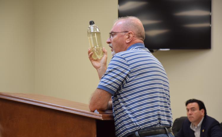 Mark Gibson shows county commissioners Monday a bottle of water taken from a polluted Indian Creek. (Photo by Scoggins)