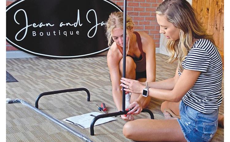 Macie Floyd and Madison Mason work together to assemble a clothing rack for their store, Jean and Jane Boutique, which is expected to open later this month. (Photo by Sinclair)
