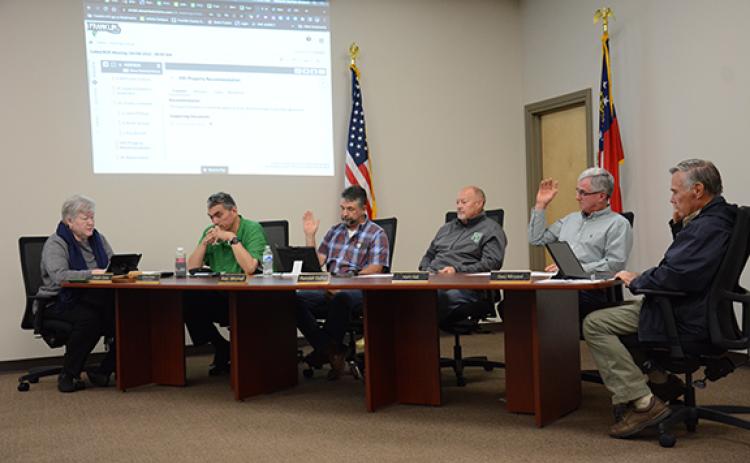 Franklin County Board of Education members Alan Mitchell, Kent Hall and Gary Minyard raise their hands to vote to purchase more than 120 acres of property just south of Carnesville as the site for a new school to replace Royston Elementary School. Fellow board members Robin Cato and Randall Gailey voted against the motion, as Superintendent Chris Forrer looked on. (Photo by Scoggins)