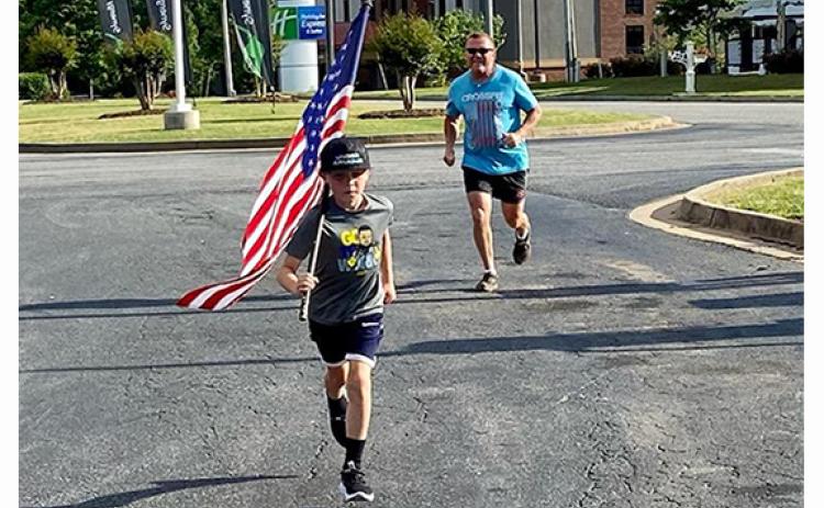 Shiloh Morgan carries the flag in front of his fa-ther Dusty during a Memorial Day run last year around Lavonia.