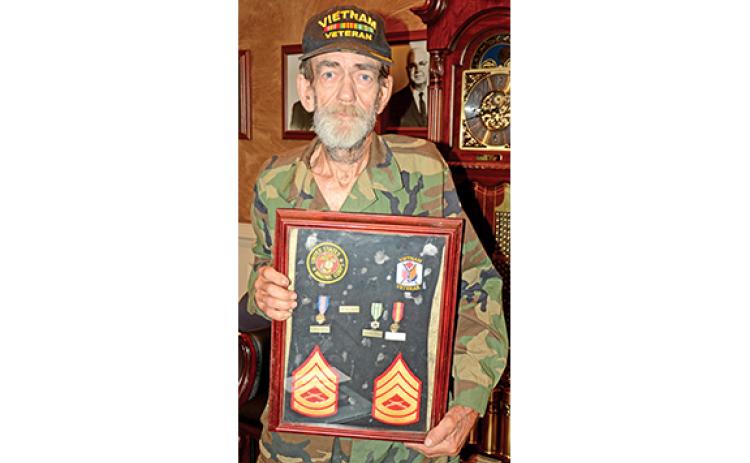 John McCollum holds a frame containing some his medals and patches from his service in the Vietnam War. (Photo by Scoggins)