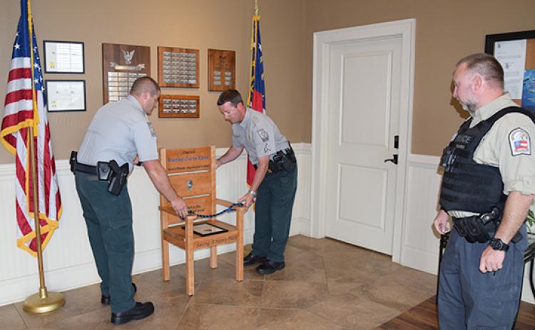 Georgia Department of Natural Resources officers place Capt. Stan Elrod’s honor chair between the flags in the lobby of Franklin Springs  City Hall as Officer-in-Charge Kevin Thompson looks on. (Photo by Sinclair)