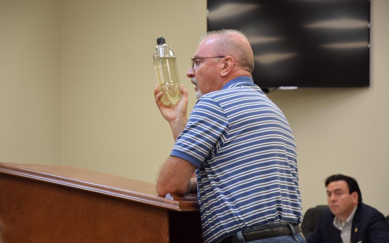 Mark Gibson shows county commissioners Monday a bottle of water taken from a polluted Indian Creek. (Photo by Scoggins)