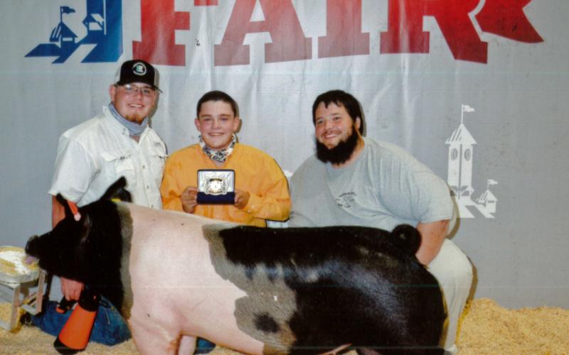 Devin Bowyer (center, with FCHS ag teacher Trey Harris at right) is one of the students who has benefited from being able to leave his pig project at the ag barn at Franklin County High School. Bowyer, one of the barn’s student managers, began showing pigs two years ago and won Senior Showmanship recently at the Georgia National Fair. A new ag barn that will allow more students to keep their pigs, sheep, goats and calves at school will be funded if voters choose to extend a special purpose local option sale